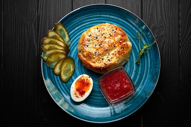 Carne, empanadas con carne y semillas de sésamo, en un plato, sobre una pizarra, con salsa y encurtidos.