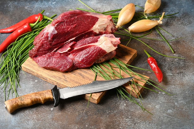 Carne escura fresca com ingredientes para cozinhar na tábua de madeira marrom.