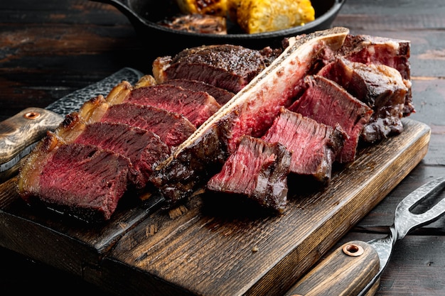 Carne fresca a la brasa. Filete de ternera a la parrilla conjunto medio raro, t hueso o corte porterhouse, sobre tabla de servir de madera, sobre fondo antiguo de mesa de madera oscura.