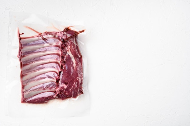 Carne fresca de costilla de cordero sellado al vacío, sobre fondo de mesa de piedra blanca, vista superior plana, con espacio para copiar texto