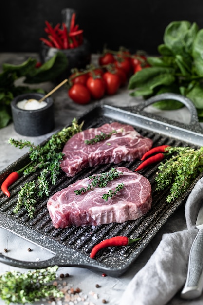 Carne fresca crua. Bife a dois com ingredientes em uma panela, com temperos, legumes e ervas