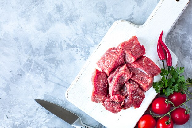 Carne fresca crua com ervas e tomates em fundo de mármore branco. vista do topo. copie o espaço. preparação de alimentos, cozinhando o conceito.