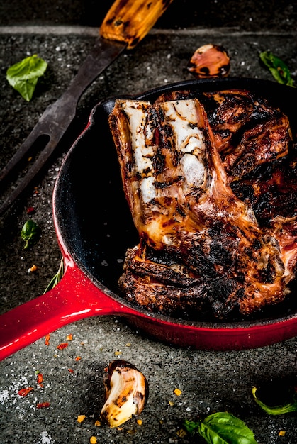 Carne fresca crua, cordeiro assado ou grelhado ou costelas com molho de tomate vermelho, pimenta, alho e especiarias na frigideira no fundo escuro de pedra, copie o espaço