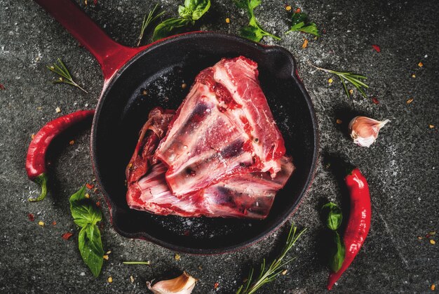 Carne fresca crua, cordeiro cru ou costelas com pimenta, alho e especiarias na frigideira frigideira em fundo escuro de pedra