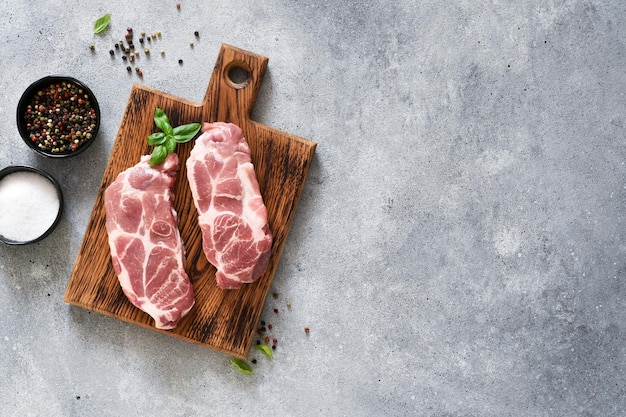 Carne fresca cruda. Filetes de cerdo con especias y albahaca sobre una tabla de madera, vista superior.