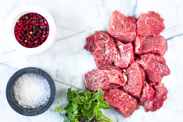 Carne fresca cruda con sal, pimienta y hierbas sobre fondo de mármol blanco. vista superior. Concepto de cocina de preparación de alimentos