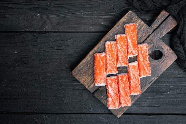 Carne fresca de caranguejo surimi com conjunto de caranguejo nadador azul, em uma tábua de madeira, no fundo preto da mesa de madeira, vista de cima plana, com copyspace e espaço para texto