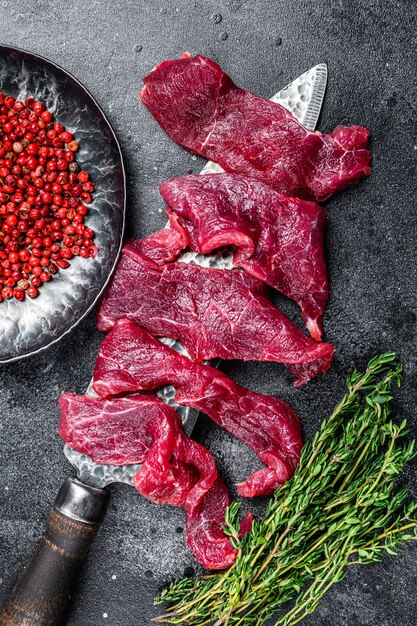 Carne fresca marmorizada cortada em tiras finas para goulash. fundo preto. vista do topo.