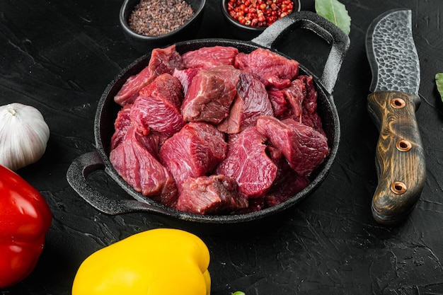 Foto carne fresca picada cruda con pimiento dulce, en una sartén de hierro fundido, sobre fondo de piedra negra