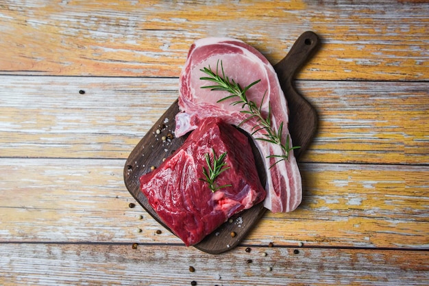 Carne fresca de res en rodajas y chuletas de cerdo especias de hierbas romero en fondo de tabla de cortar de madera bistec de carne cruda