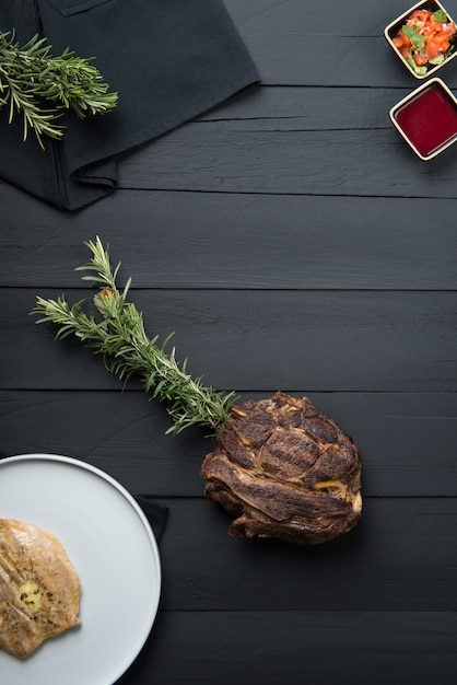 Carne frita com verduras, molho e molho sobre fundo preto de madeira