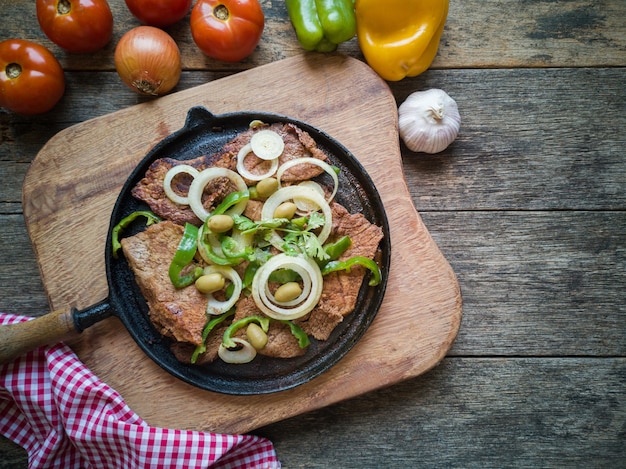 Carne frita en la placa de hierro con mesa de madera rústica Endecha plana.