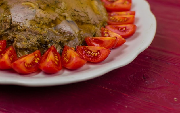 Una carne en gelatina en un plato redondo decorado con tomates sobre una superficie de madera de un puerto de color leonado