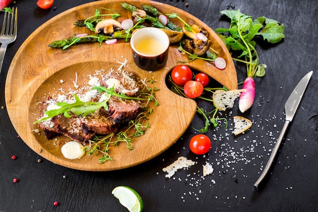 Carne grelhada com legumes na chapa de madeira em fundo preto