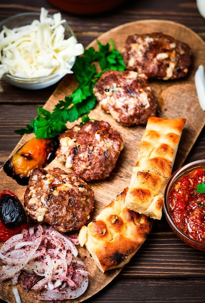 Carne grelhada. Foco seletivo do close-up. Bolinhos de carne ou costeletas - Kofte turco feito de cordeiro e boi com queijo e especiarias. Em uma travessa de madeira com legumes grelhados, ervas e molho.