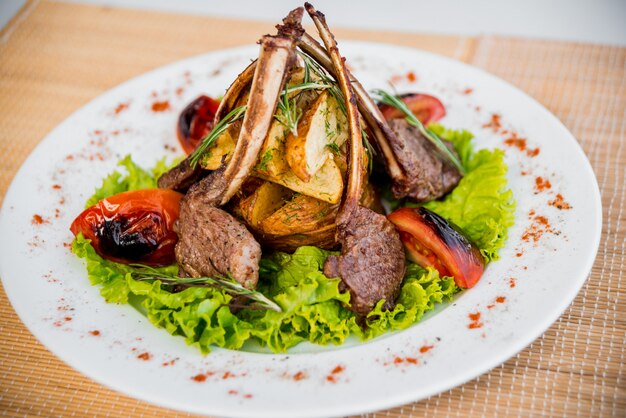 Carne en el hueso con verduras en un plato blanco.