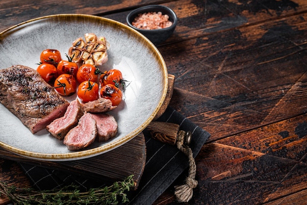 Carne de lomo de cordero asado en plato con tomate y ajo a la parrilla, filete de solomillo de cordero. fondo oscuro Vista superior. Copie el espacio.