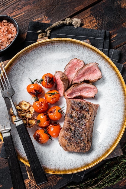 Carne de lomo de cordero asado en plato con tomate asado y filete de solomillo de cordero con ajo Fondo oscuro Vista superior