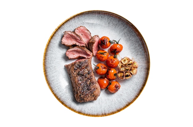 Carne de lomo de cordero asado en un plato con tomate asado y filete de solomillo de cordero al ajillo aislado de fondo blanco