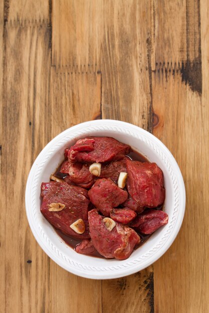 Carne marinada en plato blanco sobre superficie de madera