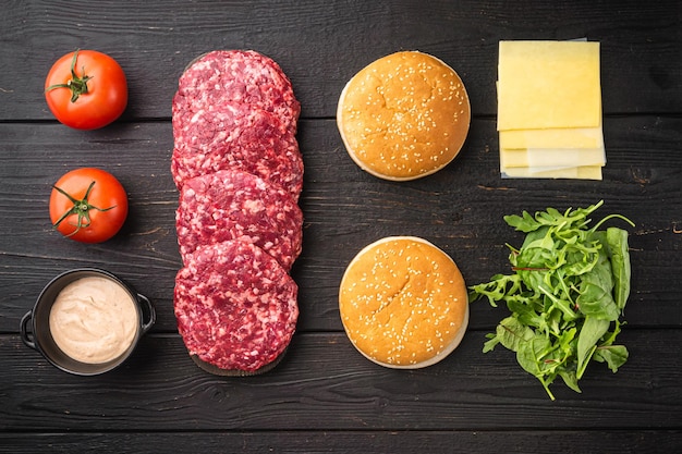 Foto carne moída crua costeletas de bife de hambúrguer e temperos com conjunto de pães, sobre fundo de mesa de madeira preta, vista superior plana