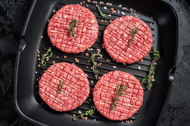 Carne moída crua Costeletas de bife de hambúrguer em frigideira grelhada pronta para cozinhar Fundo preto Vista superior