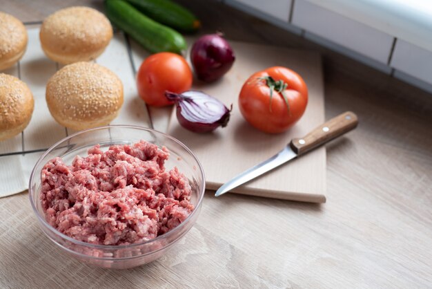 Carne molida en un recipiente de vidrio sobre la mesa de la cocina con otros ingredientes para hamburguesas