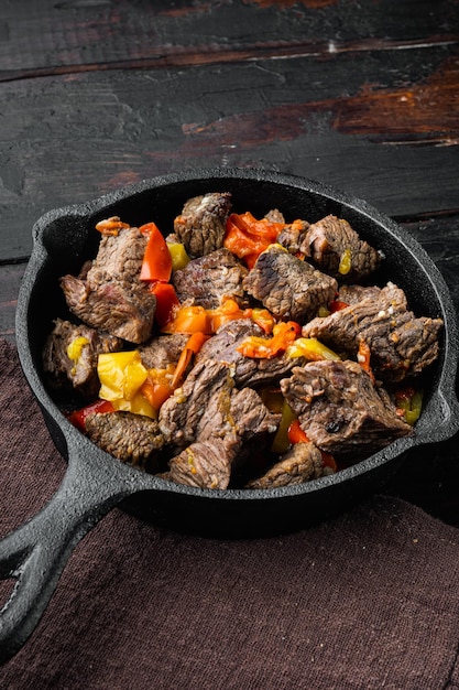 Foto carne mongol, trozos de carne guisada en salsa de soja, en una sartén de hierro fundido, sobre la vieja mesa de madera oscura.