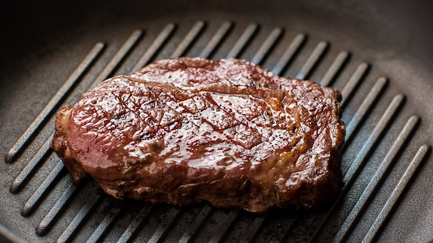 Carne na frigideira. Pedaço de carne de cor escura. Bife de Ribey cozido no restaurante. Carne suculenta deliciosa.