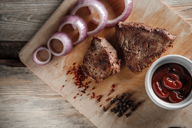 Carne a la parrilla con especias y salsa de tomate sobre un fondo de madera desgastada