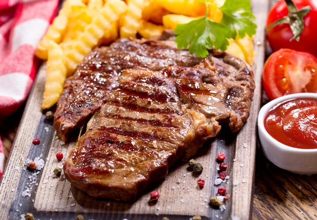 Carne a la parrilla con papas fritas en tablero de madera