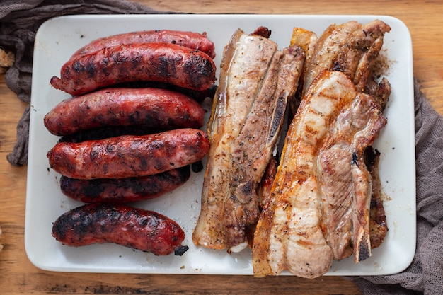 Carne a la parrilla y salchichas en un plato sobre fondo de madera