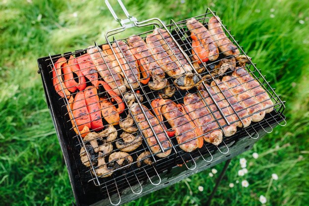 Carne a la parrilla y salchichas con verduras y especias en un brasero Vista superior Surtido de deliciosas carnes a la parrilla en parrilla con humo y llamas en hierba verde