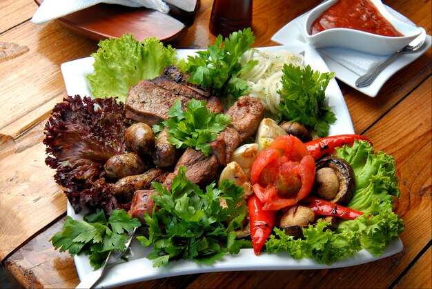 Carne a la parrilla con verduras, ensalada y salsa en un plato