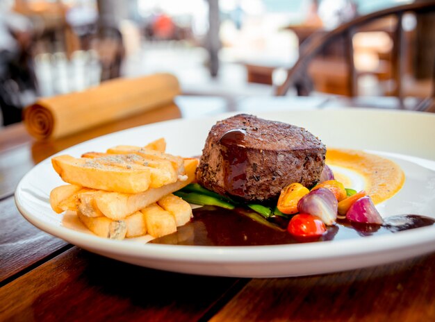 Carne con patatas fritas y ensalada vestida con salsa en un plato blanco.