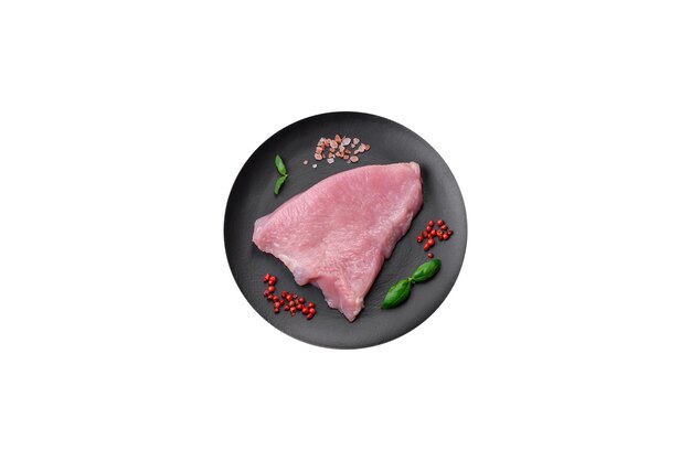 Carne de pavo cruda en forma de rodajas con sal, especias y hierbas sobre un fondo de hormigón oscuro