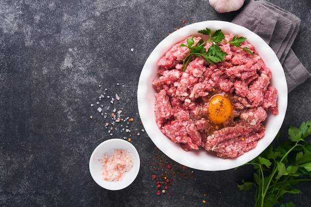 Carne picada crua carne moída carne de porco ou cordeiro especiarias ervas e ovos na chapa branca sobre fundo preto de concreto velho carne picada fresca pronta para cozinhar fundo de cozimento de alimentos vista superior