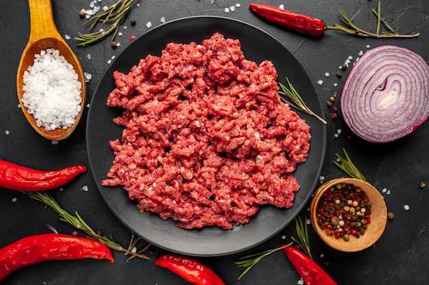 Carne picada crua fresca com ervas e especiarias em uma placa preta sobre fundo de pedra