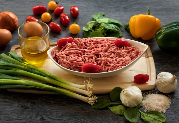 Carne picada em um prato branco com espinafre, tomate, alho e cebola em um fundo escuro de madeira