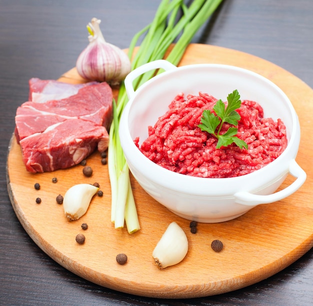 Foto carne picada em uma tigela branca com ervas e especiarias frescas em uma mesa