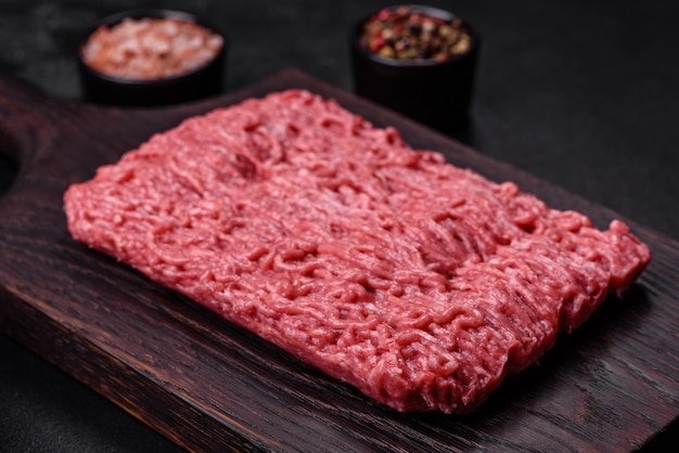 Carne picada fresca en tabla de cortar sobre fondo oscuro con ingredientes para cocinar