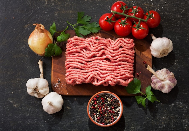 Carne picada con ingredientes para cocinar sobre tabla de madera, vista superior