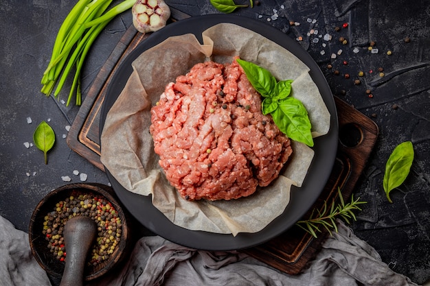 Carne picada en un plato y especias sobre un fondo negro, vista superior. Foto de alta calidad