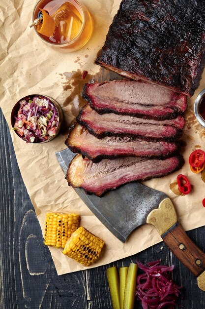 Carne de res a la barbacoa de pechuga fresca en rodajas para servir sobre un fondo de papel kraft con salsa, pimientos picantes y maíz. Alojamiento generoso para espacio de copia. estilo americano