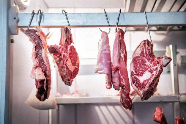 Carne de res colgando de ganchos de metal en la sala de frigorífico de carnicería