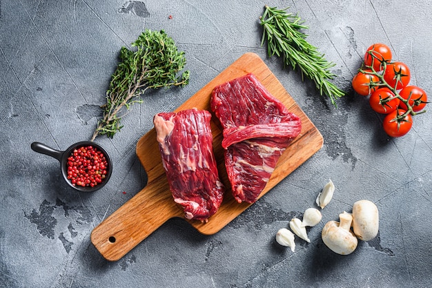 Carne de res cruda cortada sobre tabla de cortar de madera, con hierbas