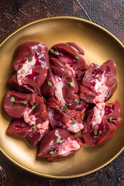 Carne de res cruda, riñón, carne fresca de despojos en rodajas en el plato, fondo oscuro, vista superior