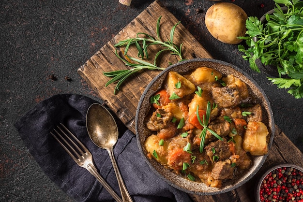 Carne de res estofada con patatas hierbas y zanahorias en un plato con una cuchara en fondo negro vista superior