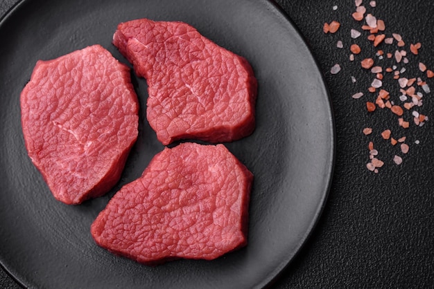 Carne de res fresca y jugosa con especias saladas y hierbas sobre un fondo de hormigón de textura oscura