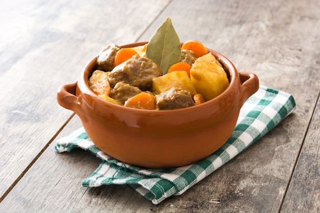 Carne de res guisada con papas, zanahorias y especias en un tazón en la mesa de madera